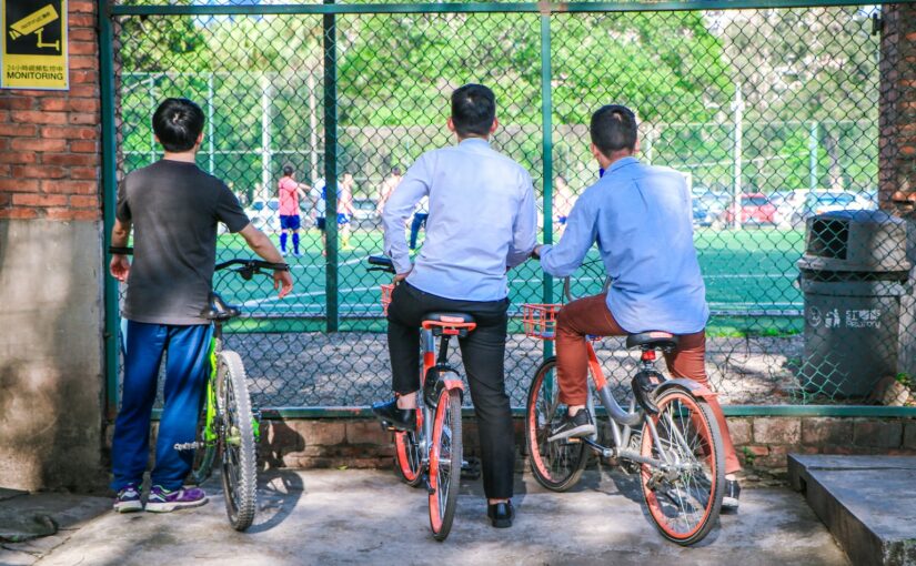 three men sitting on bikes while watching soccer game