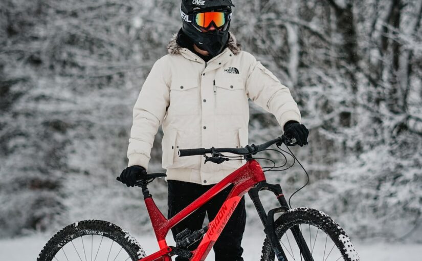 man in beige jacket riding red mountain bike on snow covered ground during daytime