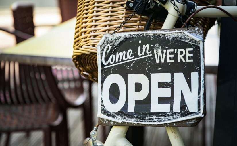 black and white come in we're open signage pinned on white bicycle with brown wicker basket at daytime