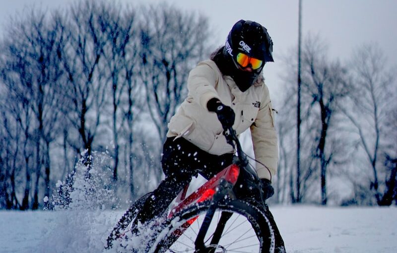 man in white jacket riding on black bmx bike on snow covered ground during daytime